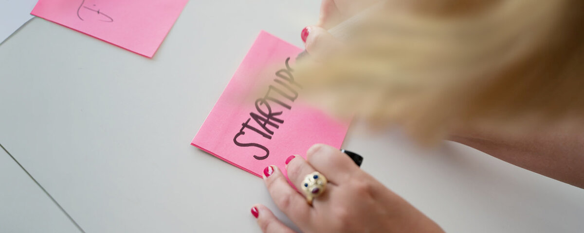 Frau schreibt das Wort Startup auf einen Postit